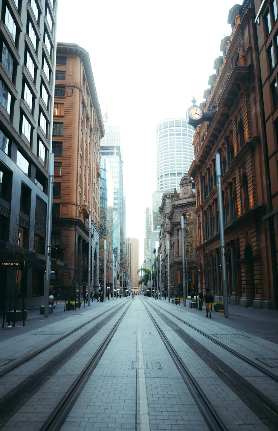 Pedestrian walks along a city street lined with historic and modern buildings.