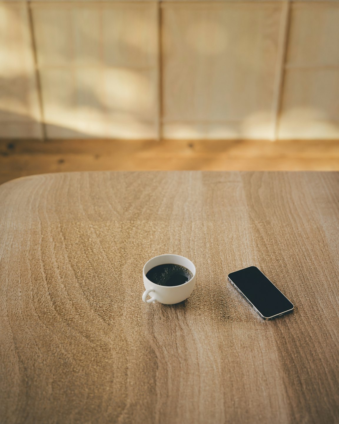 Black coffee and a smartphone rest on a wooden table.