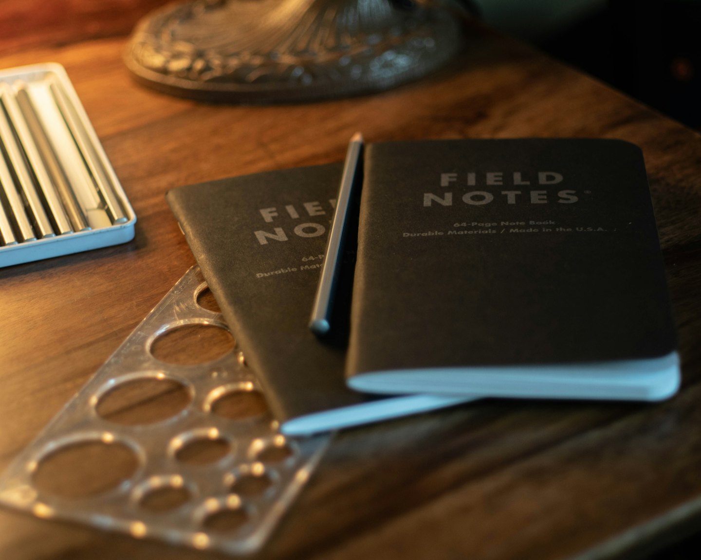 Two notebooks, metallic pens, and a template on a wooden table.
